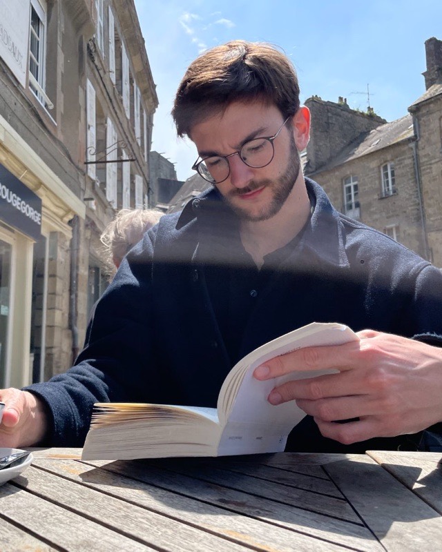 Adrien Caillo reading a book at a café terrace